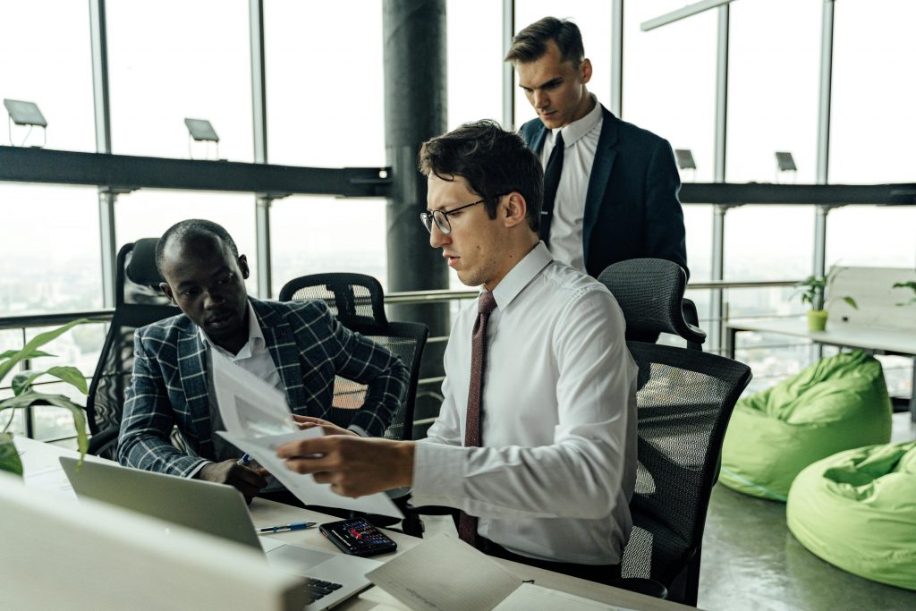 Professionals engaging in teamwork and discussion in a contemporary office setting with large windows.